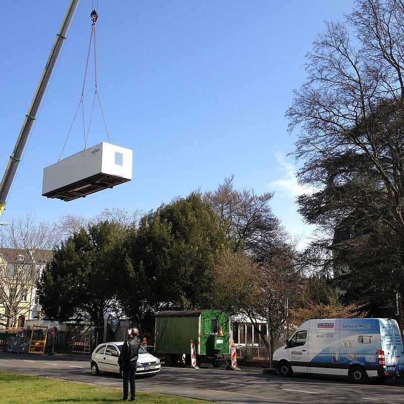 Kran hebt Küchencontainer in die Luft, um ihn zum Zelt-Container-Konstrukt hinzuzufügen.