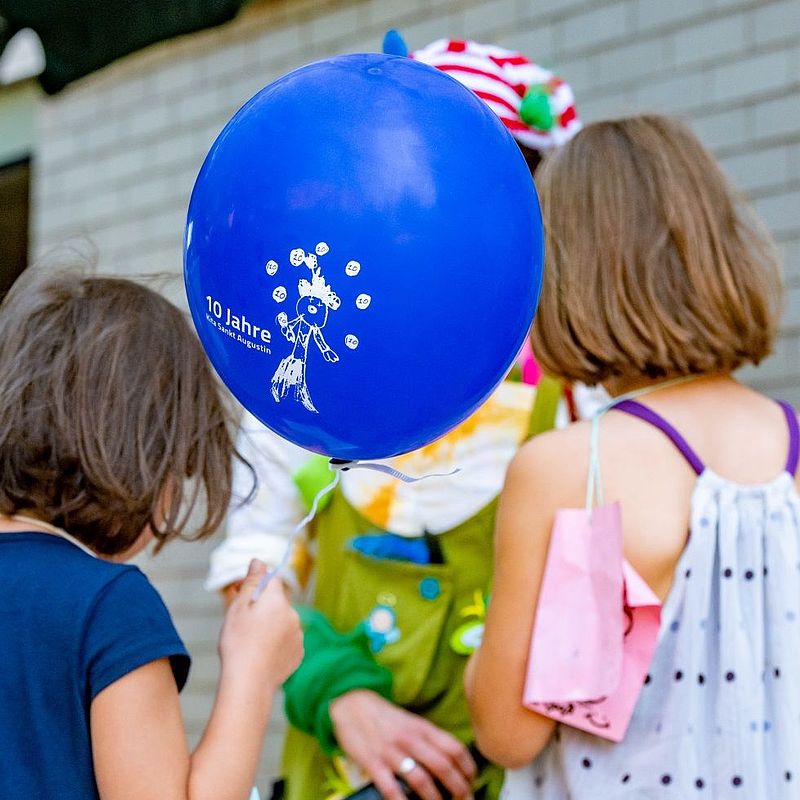 Kinder mit dem Rücken zur Kamera und einem blauen Luftballon in der Hand