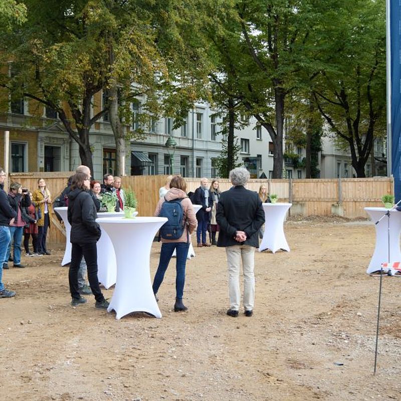 Stehtische auf dem Baufeld mit den Gästen des Spatenstiches daran, in Unterhaltungen versunken.