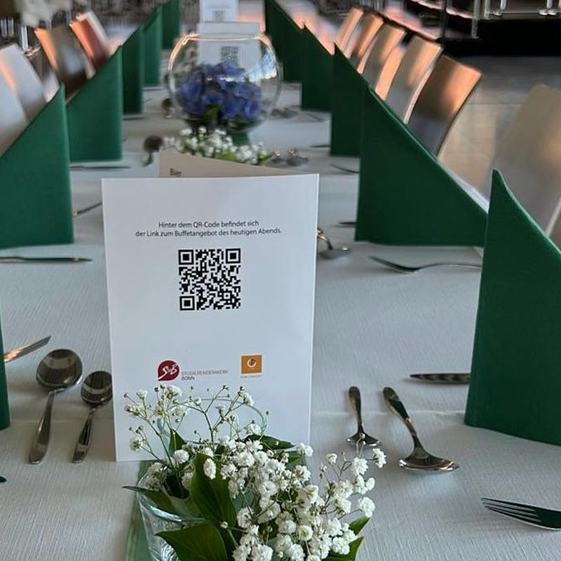 Schoen gedeckte Tischreihen mit gruenen Servietten und weißen und blauen Blumen als Tischdeko in deiner Bonner Abi-Location.