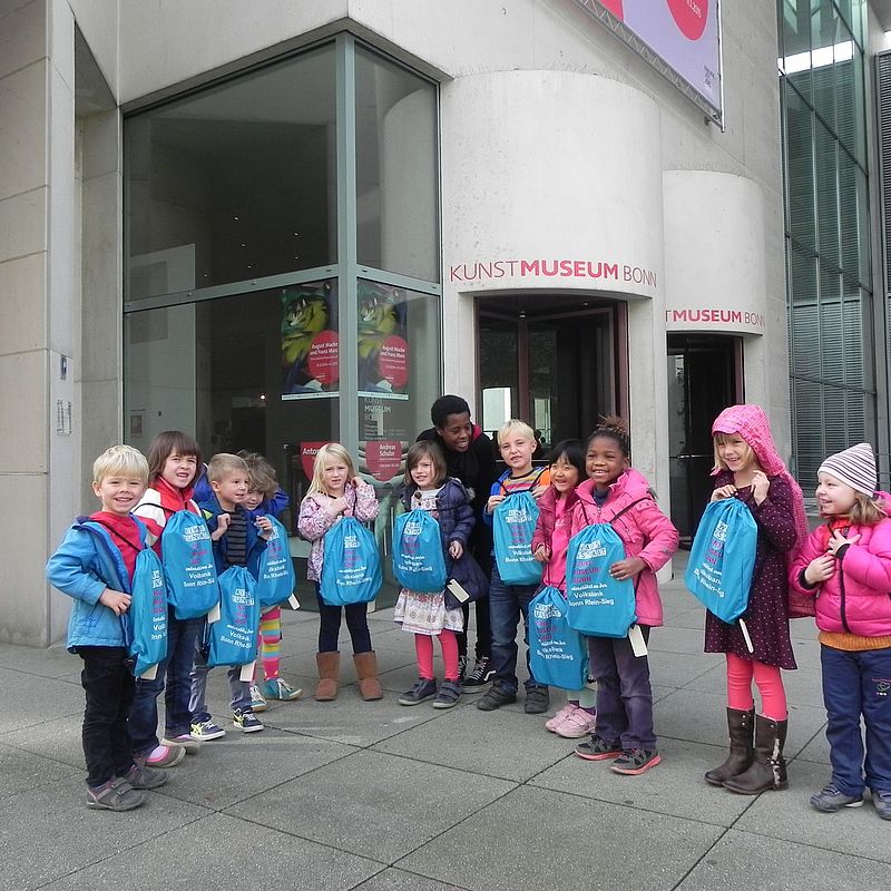 Kinder posieren vor dem Museum mit ihren Rucksäcken, die sie beim Workshop geschenkt bekommen haben