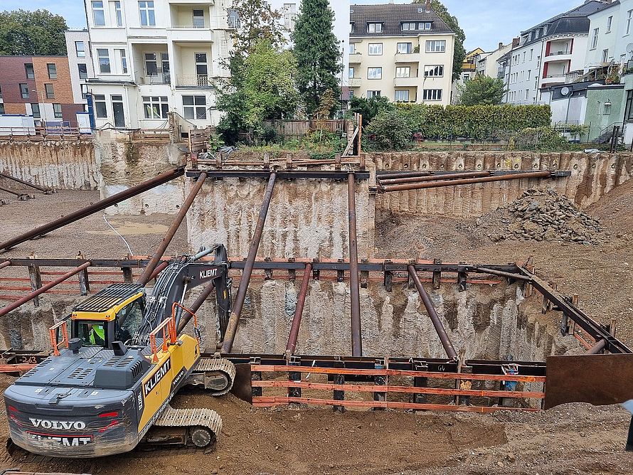 Baugrube in Wohngebiet mit abgestützten Erdwänden durch Stahlträger und einem Bagger