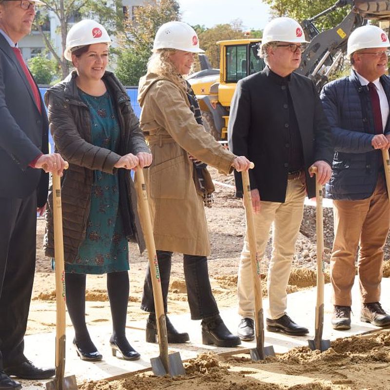 Jeder hat eine Schaufel in der Hand und sie stützen sich darauf wie auf einer Krücke ab: Madita Mues (AStA-Vorsitz), Professor Klaus Sandmann (Prorektor der Uni Bonn), Katja Dörner (Oberbürgermeisterin), Dr. Sandra Scheermesser (Ministerium für Kultur und Wissenschaft), Professor Gerd Jäger (Generalplaner Baumschlager Eberle Architekten) und Jürgen Huber (Geschäftsführer des Studierendenwerks) (von links nach rechts)