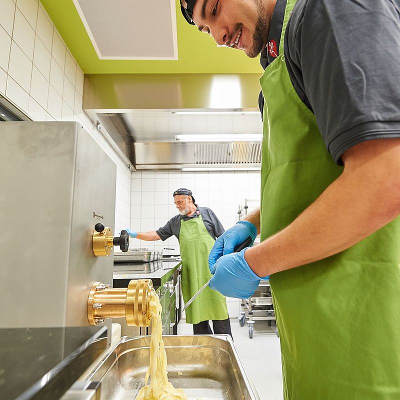Mitarbeiter der Mensa CAMPO arbeitet an der Pasta-Station und entnimmt frische Nudeln aus der Pastamaschine