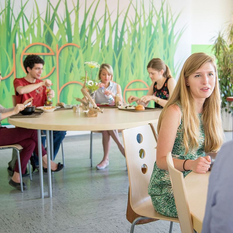 Studierende sitzen im Speisesaal und haben Essen vor sich