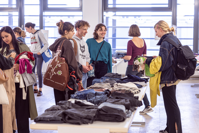 Es gibt verschiedene Gruppen von Studenten, die sich wegen der Kleidung, die dort auf den Tischen liegt, beraten.