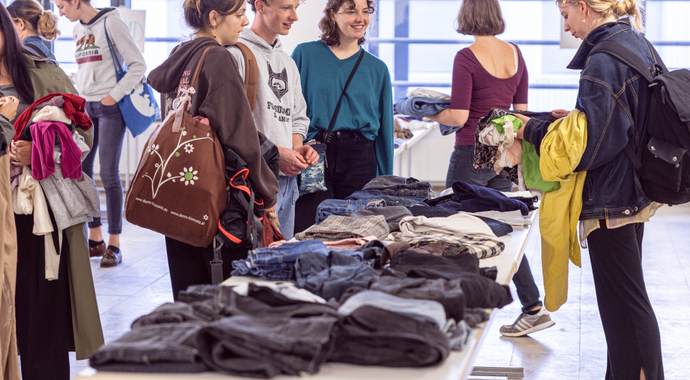 Es gibt verschiedene Gruppen von Studenten, die sich wegen der Kleidung, die dort auf den Tischen liegt, beraten.