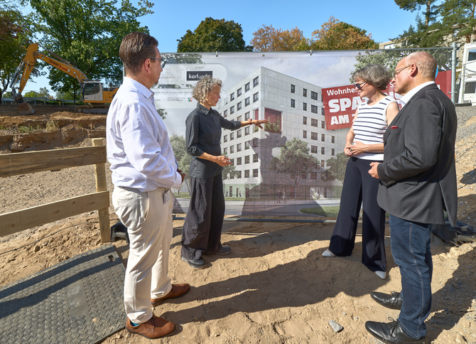 Ministerin Scharrenbach, Oberbürgermeister Deus, die Architektin und Geschäftsführer des Studierendenwerks schauen sich das Banner mit der Visualisierung des Wohnheims an.