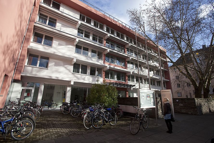 Mehrstöckiges rosa-weißes Wohngebäude mit vielen geparkten Fahrrädern und einer Person an einem Infokasten