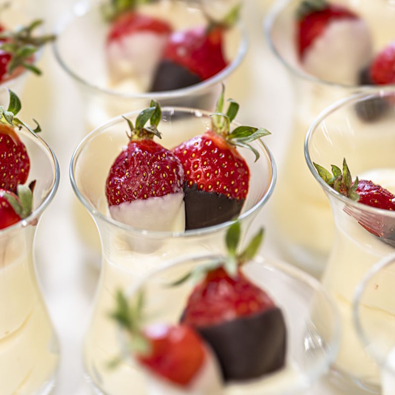 Close-up kleiner Dessert-Glaeschen mit einer weißen Creme und schokolierten Erdbeeren