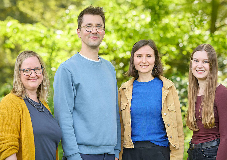 Das Team der Psychologischen Beratungsstelle steht im Botanischen Garten vor Bäumen und schaut freundlich in die Kamera.