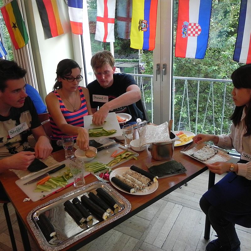 Eine japanische Studentin unterstuetzt die Teilnehmenden des Kochworkshops beim Rollen von Sushi